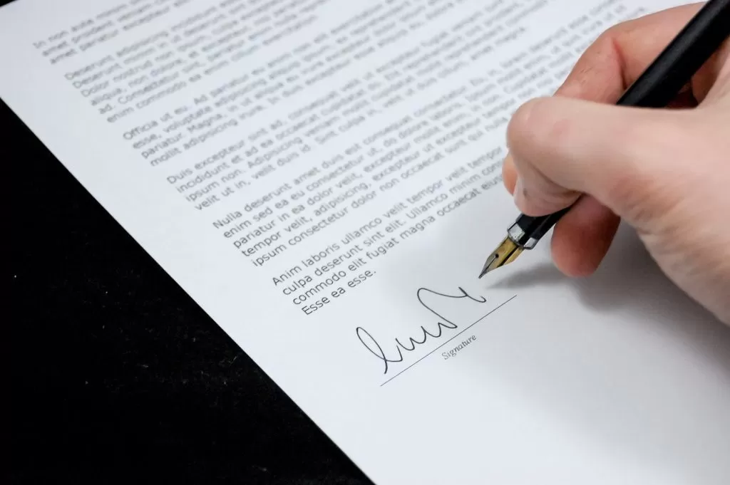 A hand signing a typed letter with a fountain pen